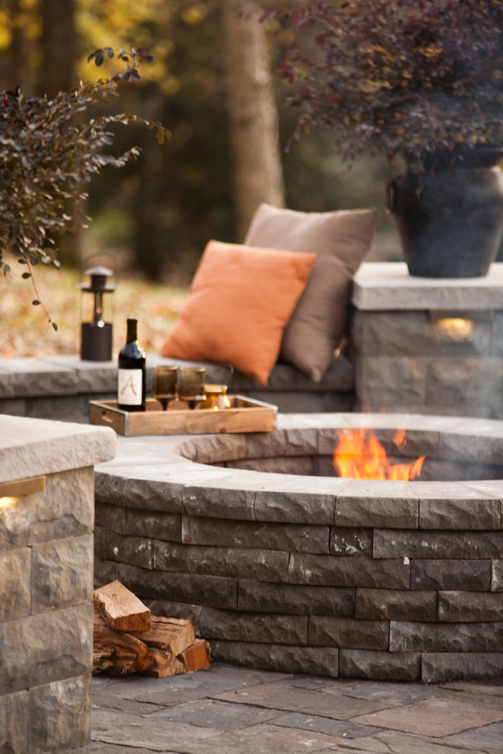 A stacked-stone fire pit with warm evening styling on a natural stone patio